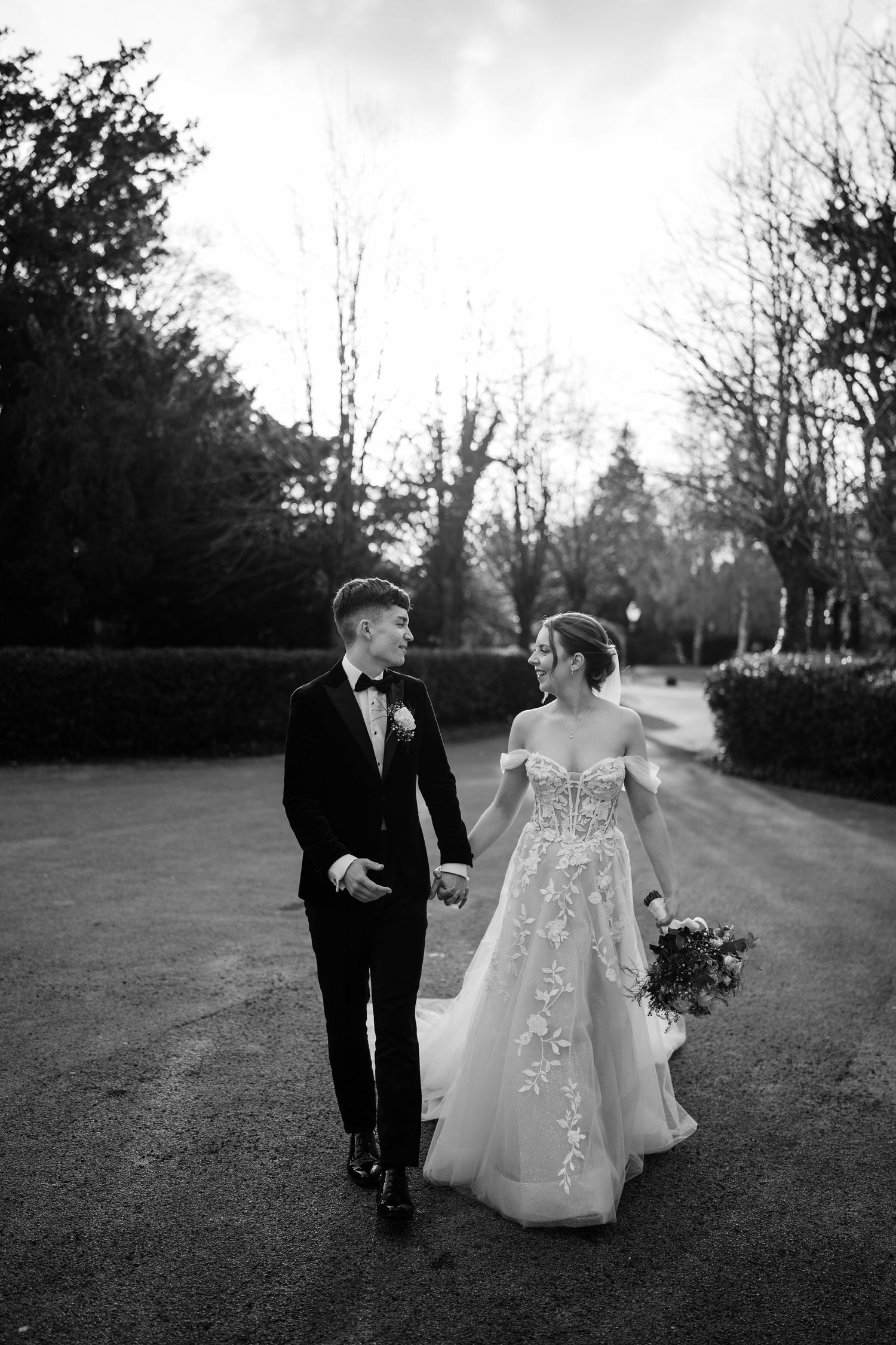 Bride and groom holding hands looking at each other as the sun sets amongst trees behind them.