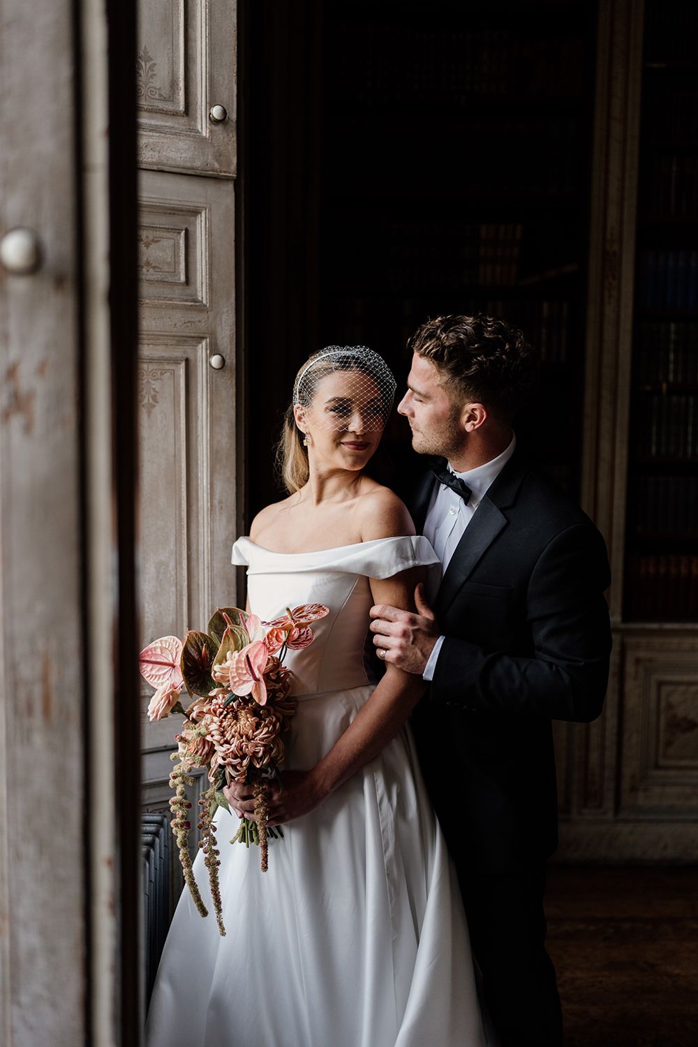 Bride and groom face towards each other while being lit by a grand window at Rise Hall.