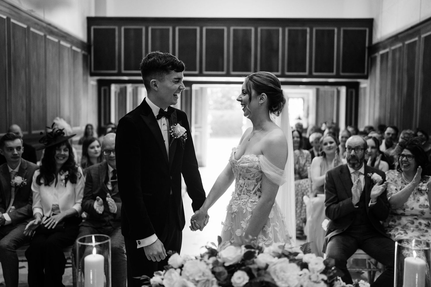 Couple getting smiling during their wedding ceremony with guests in the background.
