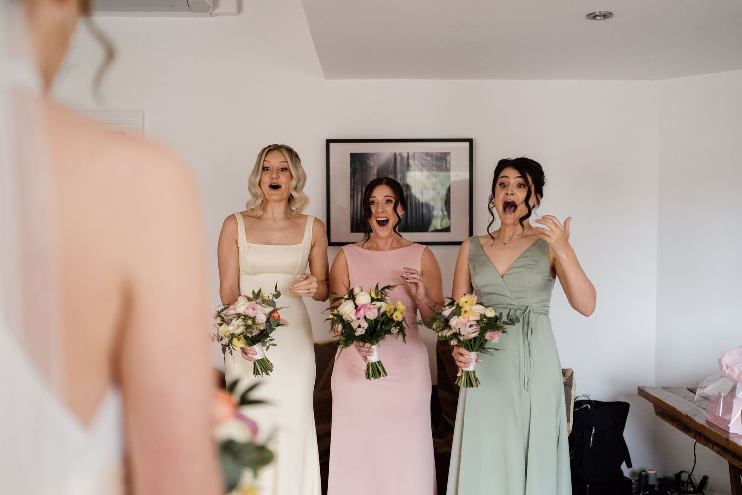 Three people in pastel dresses holding floral bouquets during a wedding celebration.