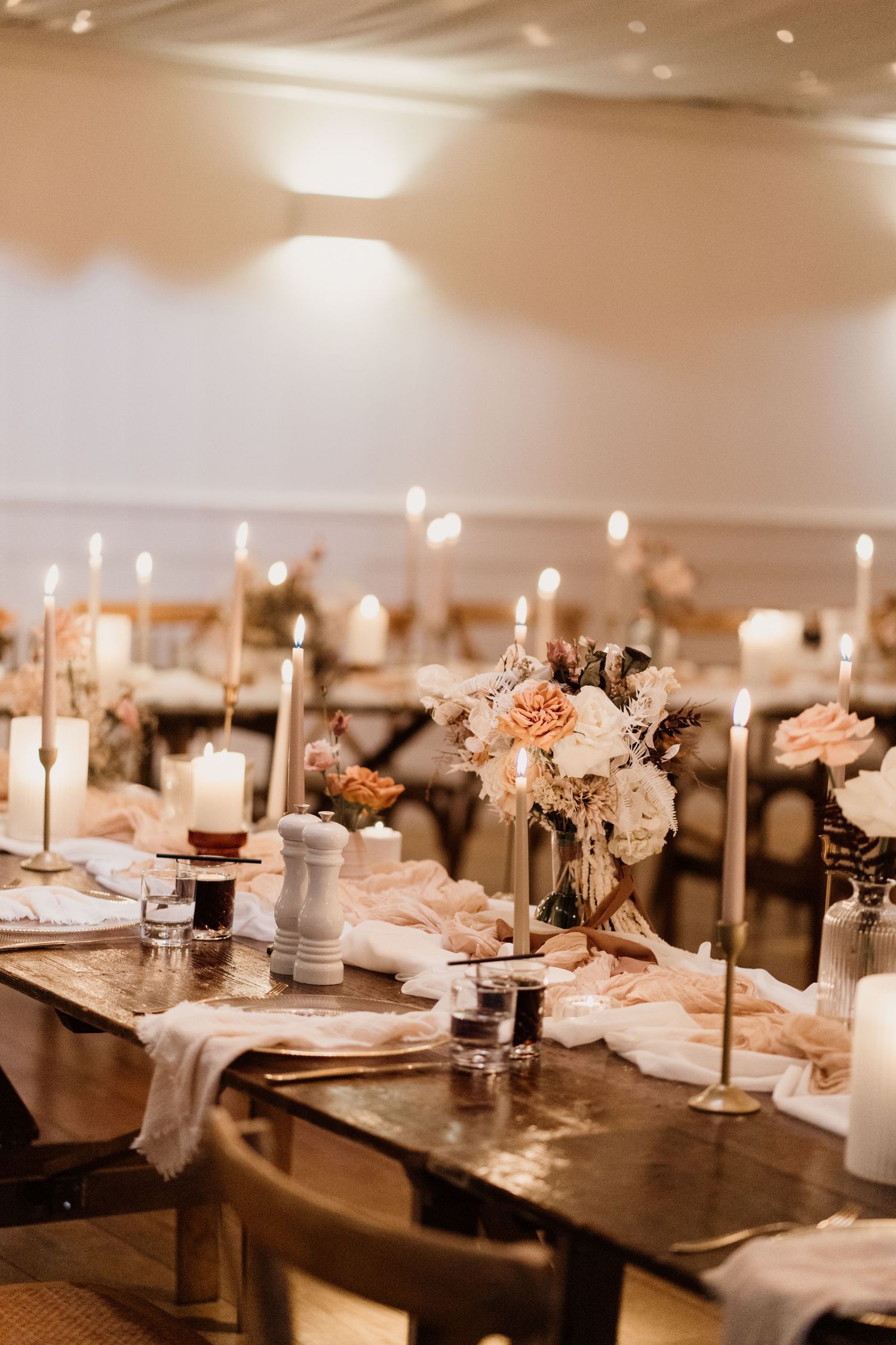 Elegant wedding reception table setting with white floral centerpieces and tall taper candles.
