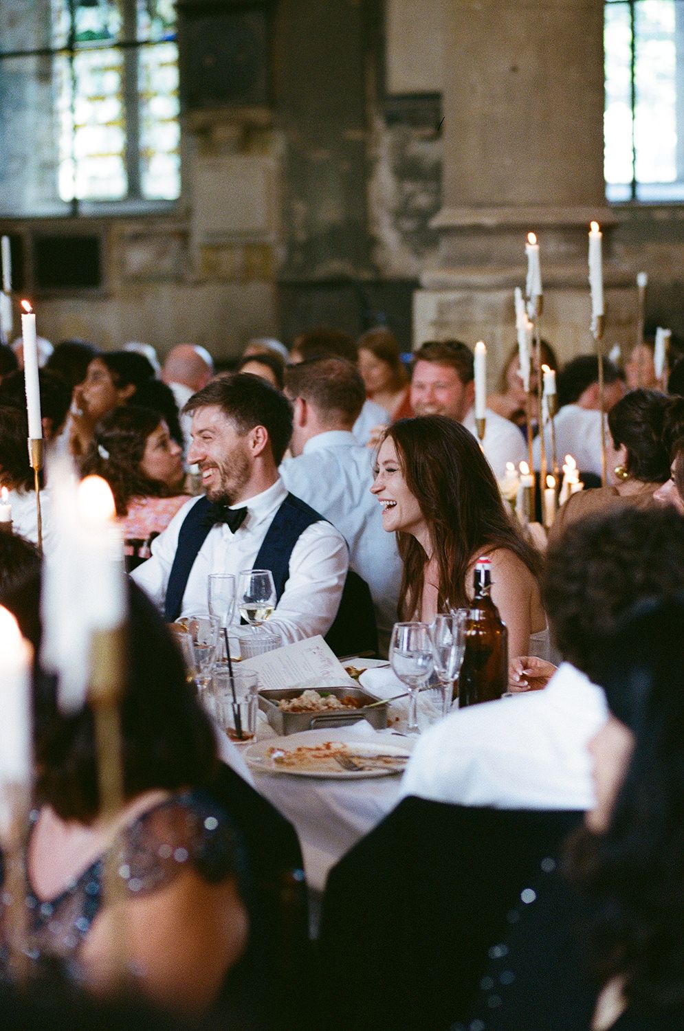 Wedding guests seated at elegant candlelit tables during an indoor reception celebration.