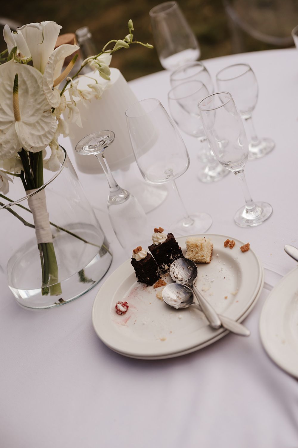 Elegant table setting with empty wine glasses, white flowers in vase, and remnants of dessert on a plate.