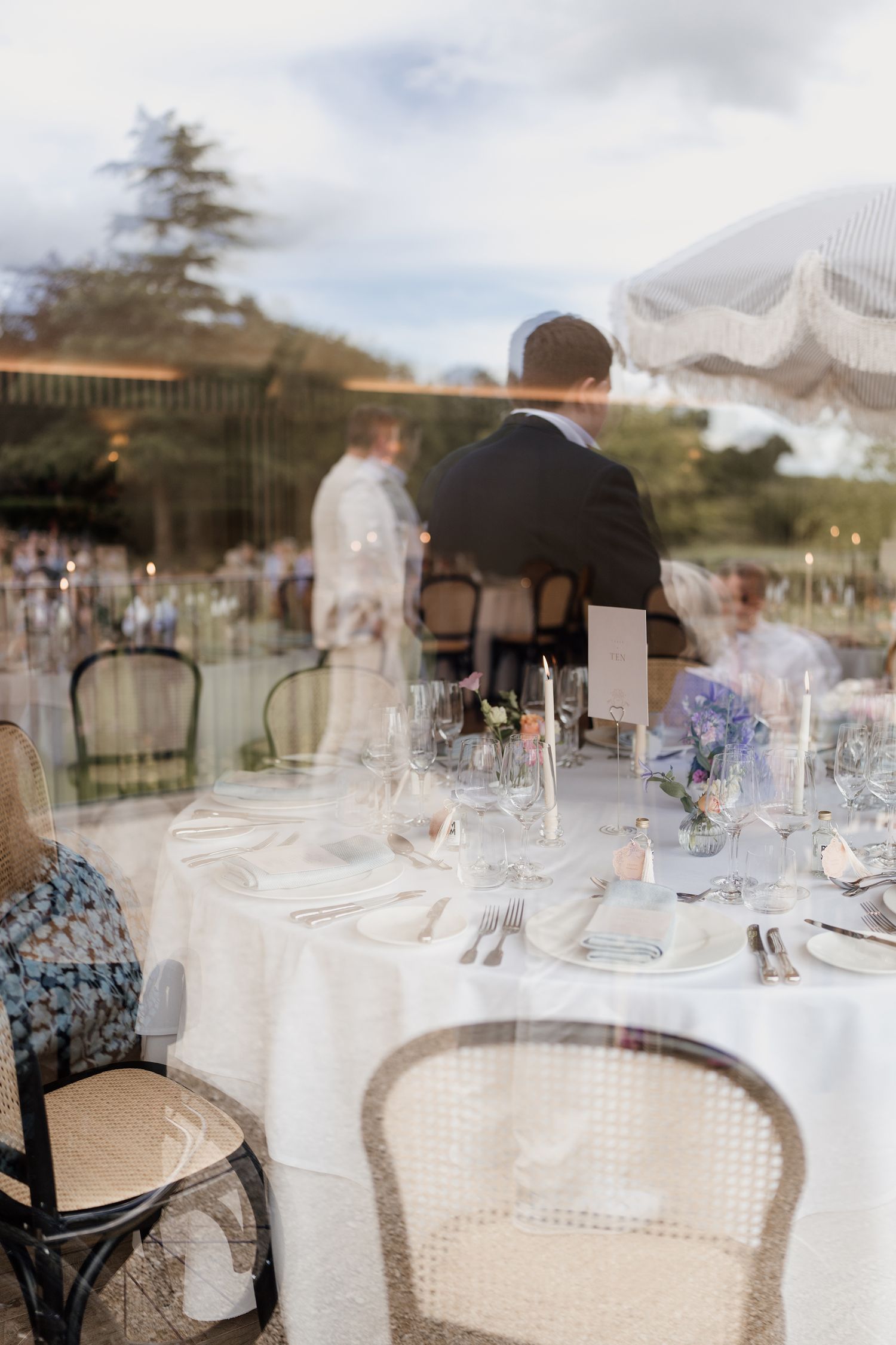 Elegant wedding reception table setting viewed through glass with floral centerpieces and candles.