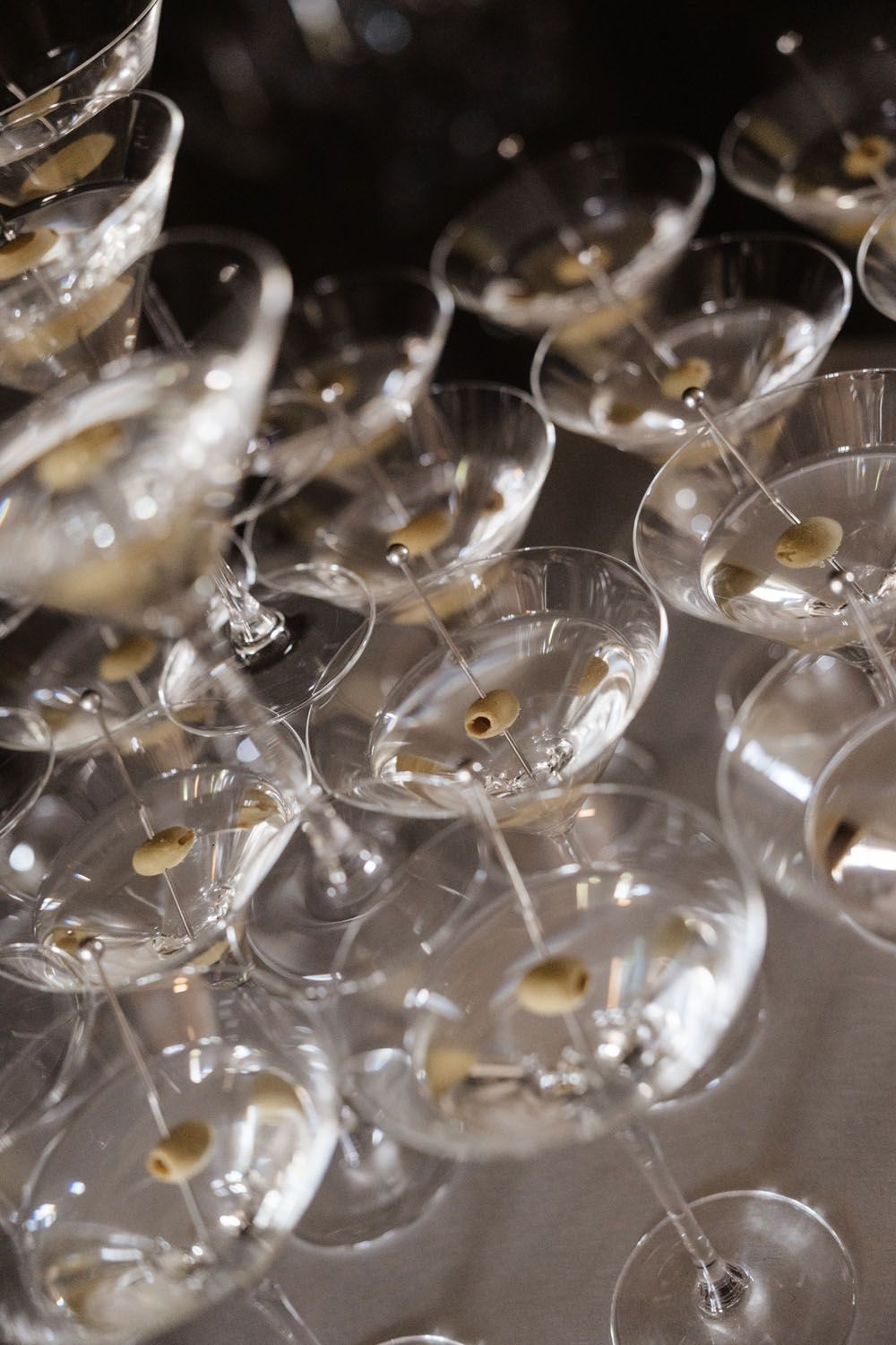 Multiple martini glasses filled with clear cocktails and green olives on picks arranged on a surface.
