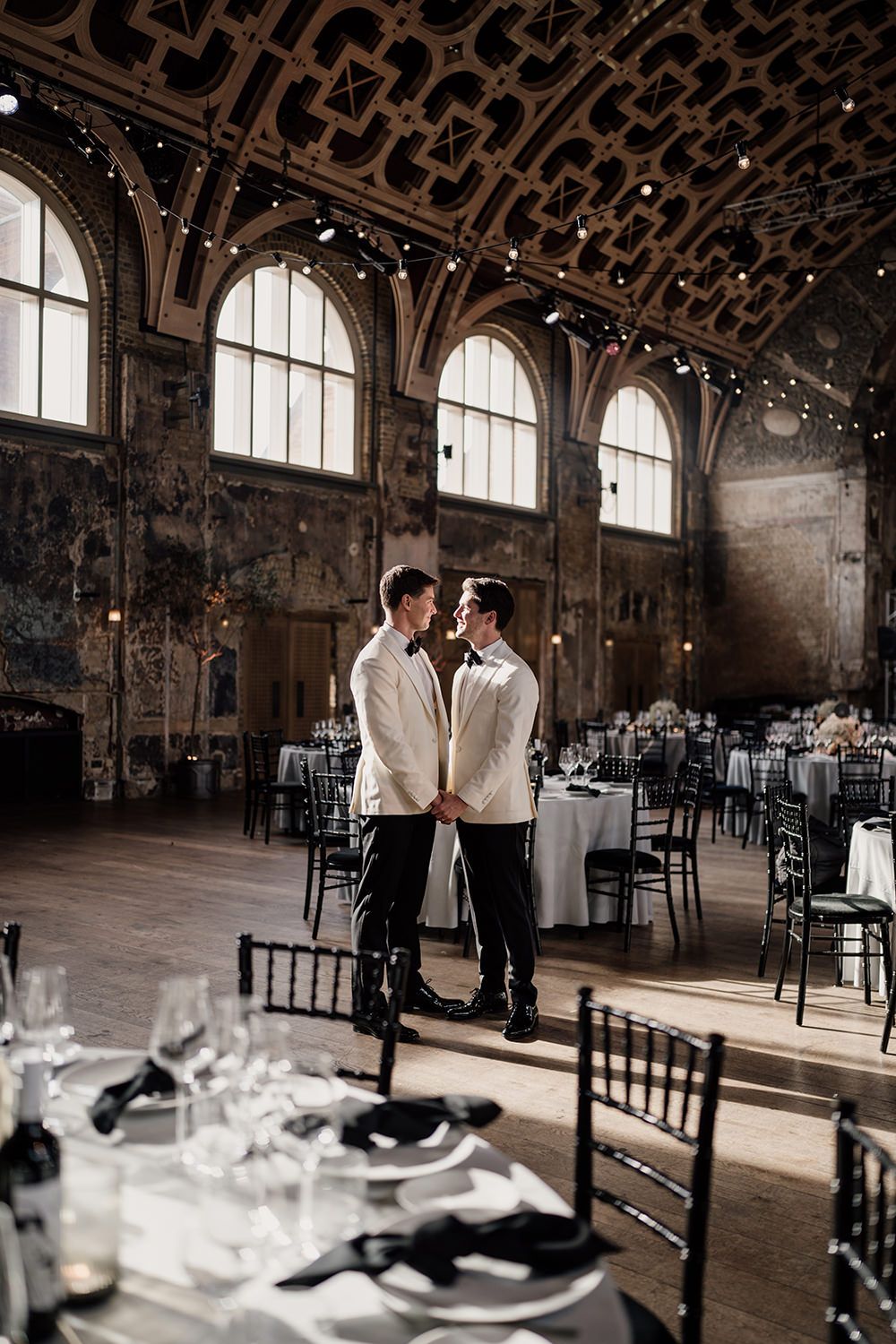 Wedding reception tables styled with monochrome colours at Battersea Arts Centre with grooms stood inbetween.