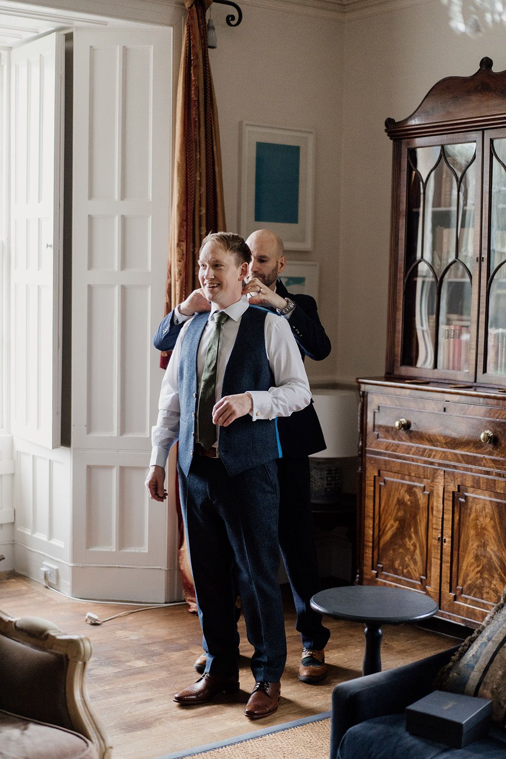 Groomsmen helping groom put on wedding suit.