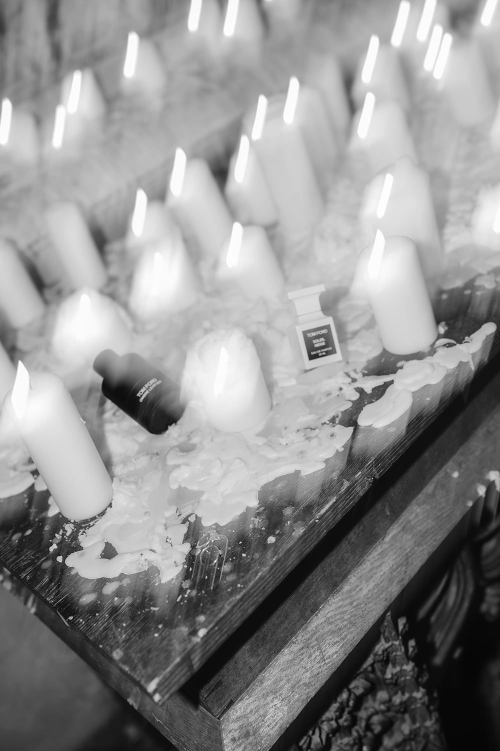 Multiple lit white candles arranged in a row on a dark wooden surface create a soft, glowing ambiance.