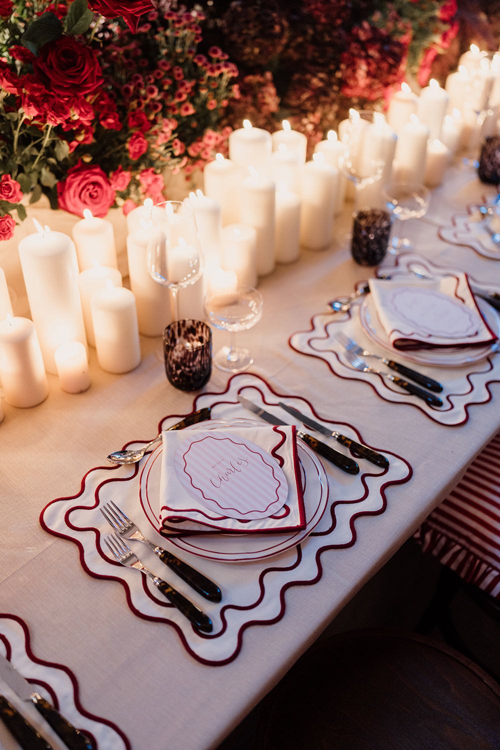 Elegant wedding table setting with white paper placemats, candles and red roses creating a romantic ambiance.