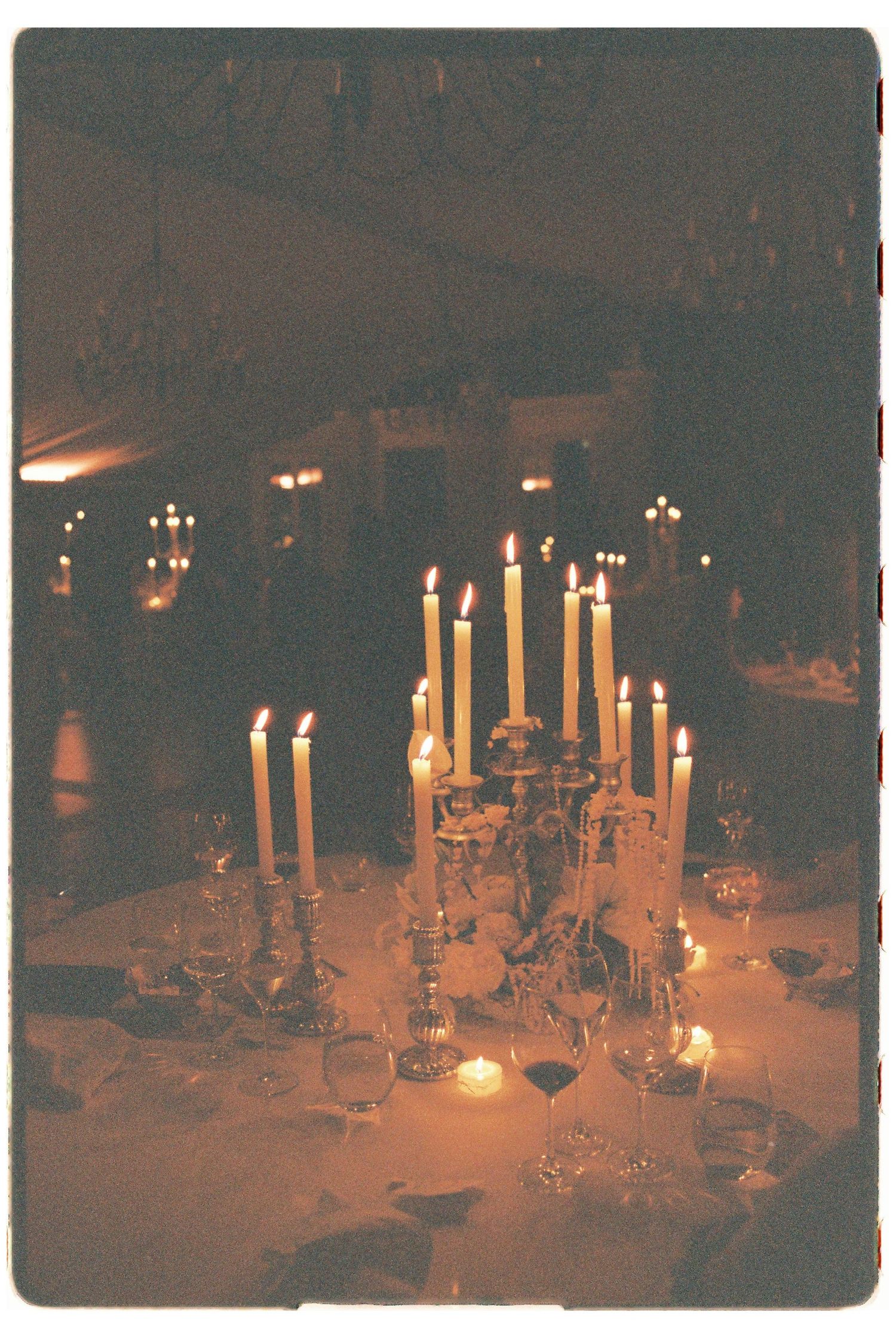 Romantic candlelit wedding reception table adorned with tall taper candles and crystal glassware in warm light.