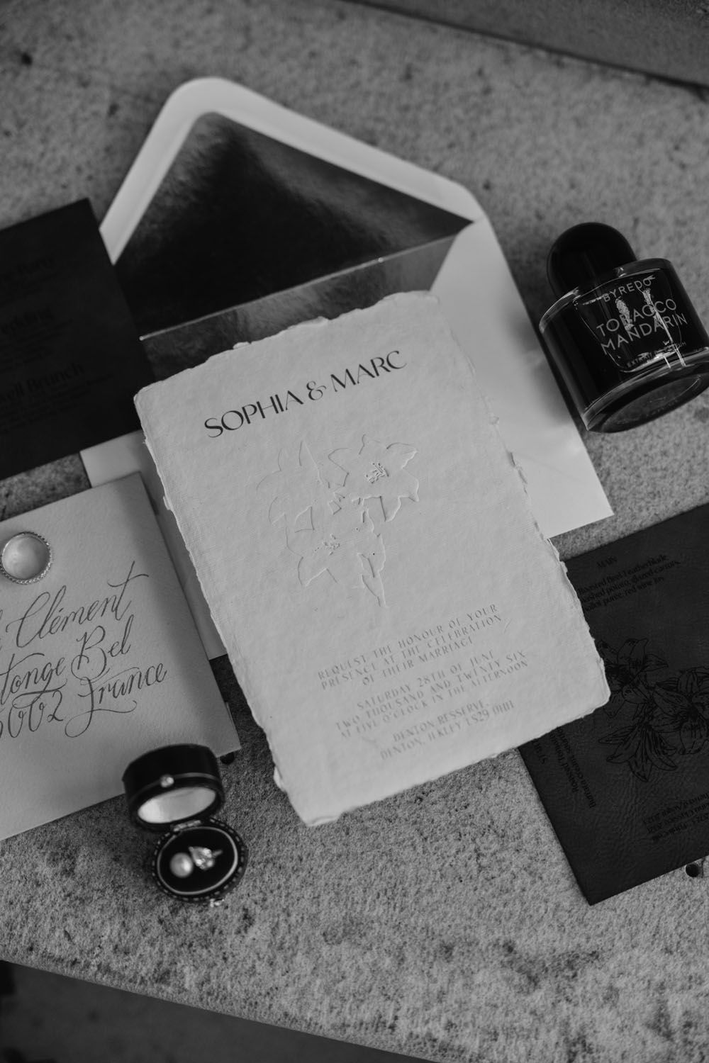 Black and white flat lay of elegant wedding stationery for Sophia and Marc with ink bottle and rings.