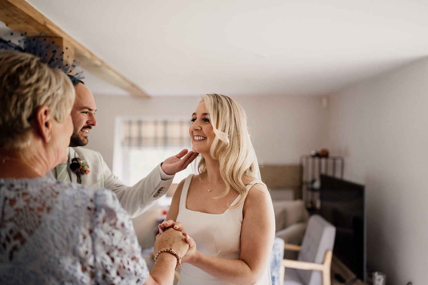 Bride smiling as she holds hands with her mam and brother touches her hair.