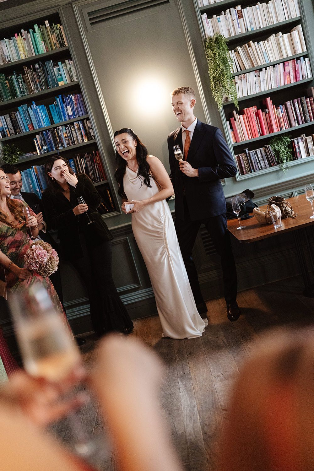 A sequence of candid moments captured during a celebration in a library setting with bookshelves in the background.