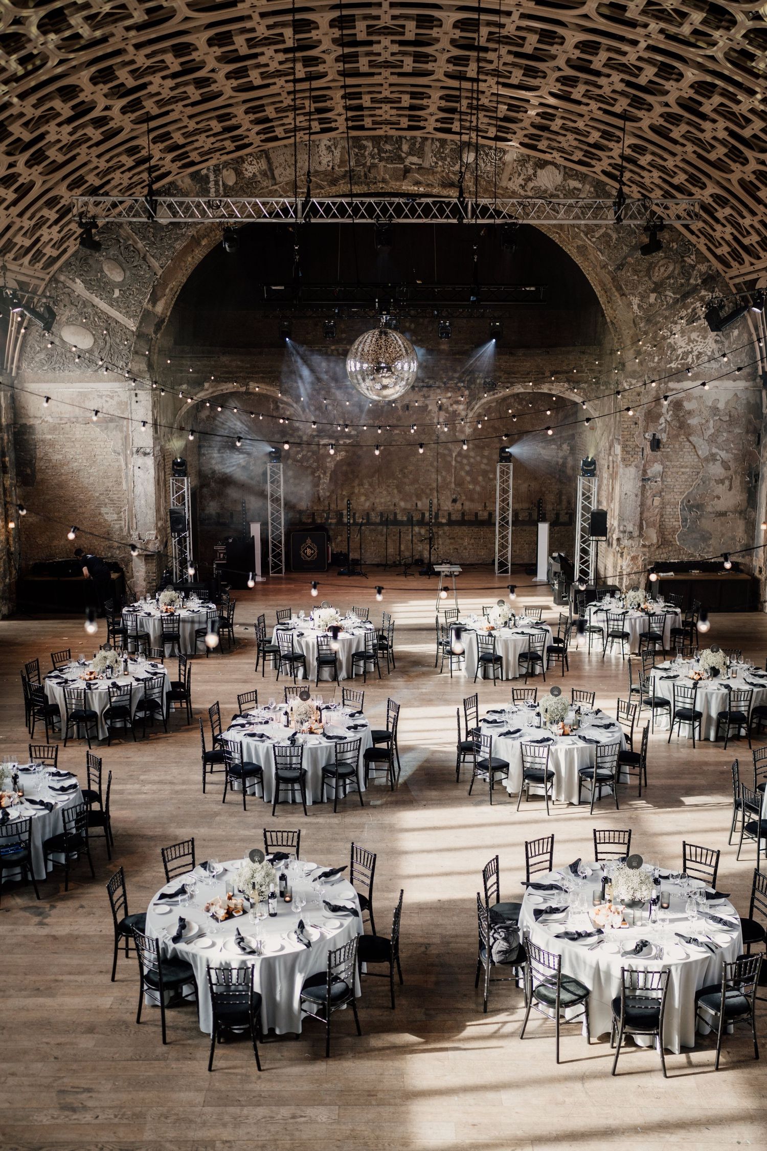 Grand wedding reception hall with arched stone ceiling, round tables, and disco ball lighting.