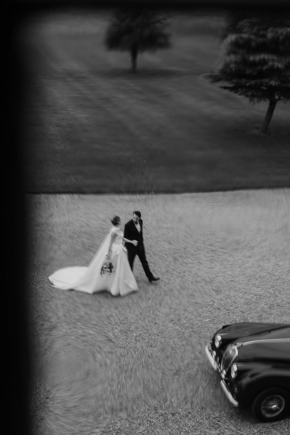 Bride and groom walking through the grounds at Rise Hall with their vintage car.