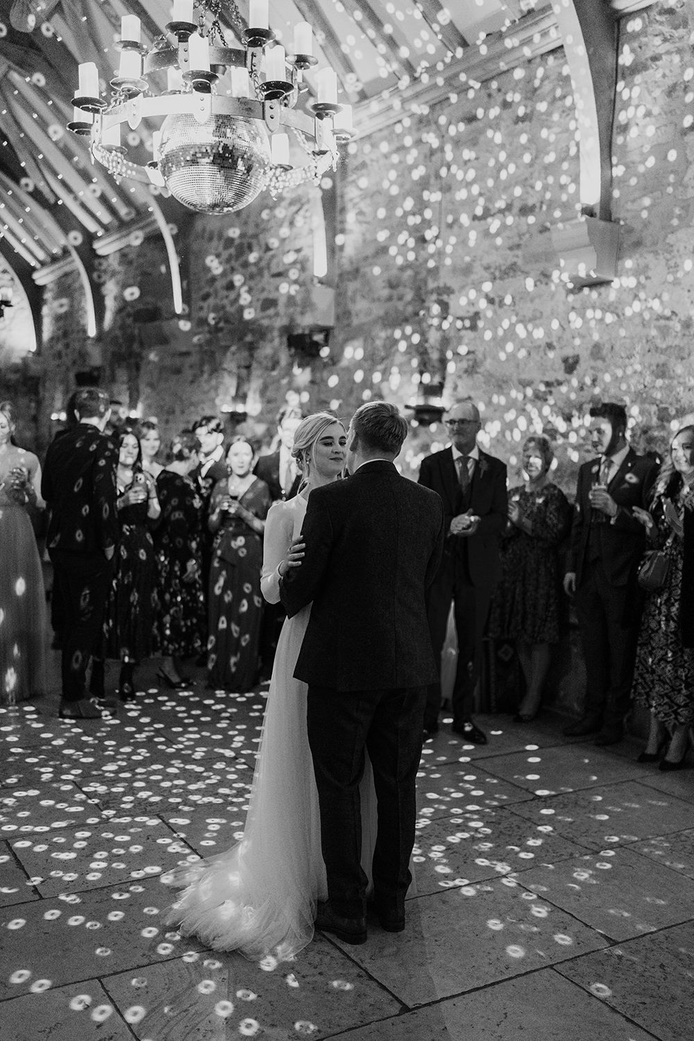 Bride and groom dancing under the disco ball at Healey Barn with guests watching stood in a circle in black and white.