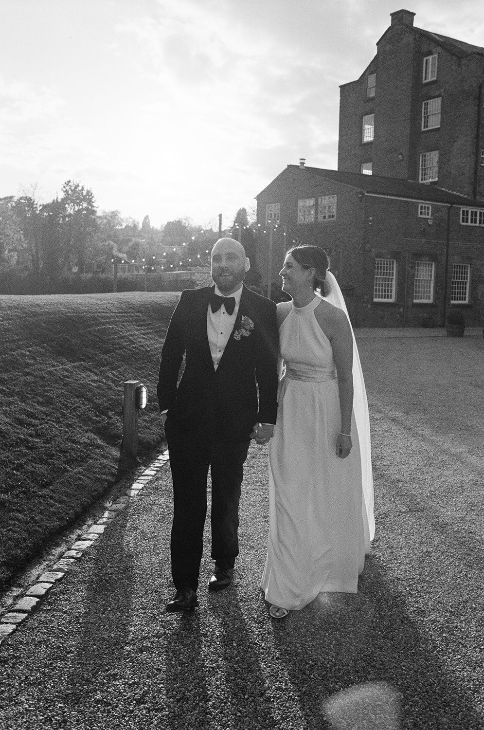 Bride and groom walking and laughing at sunset with The West Mill and River Derwent behind them.