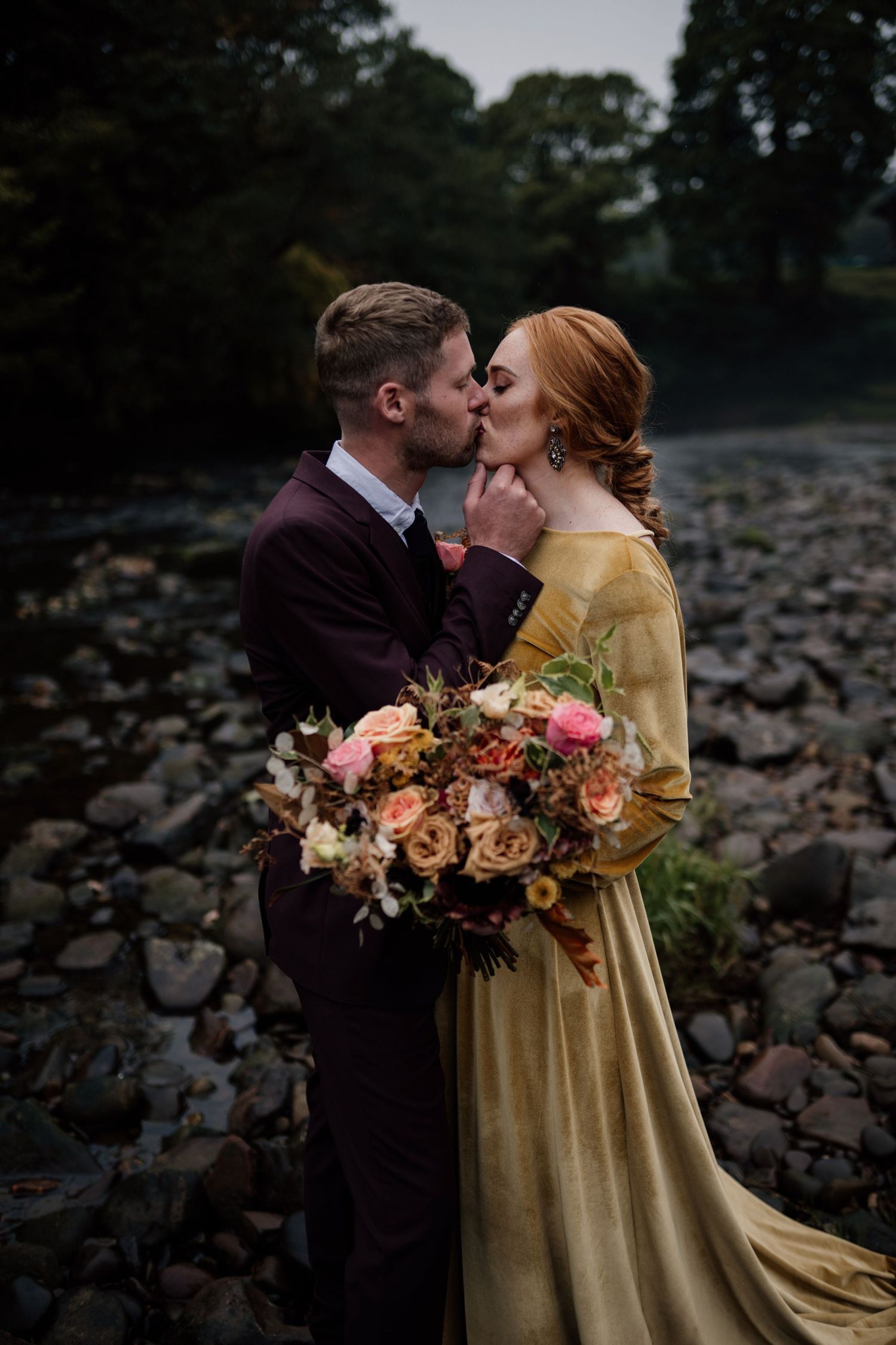 Couple kissing while wearing autumnal coloured wedding clothes.