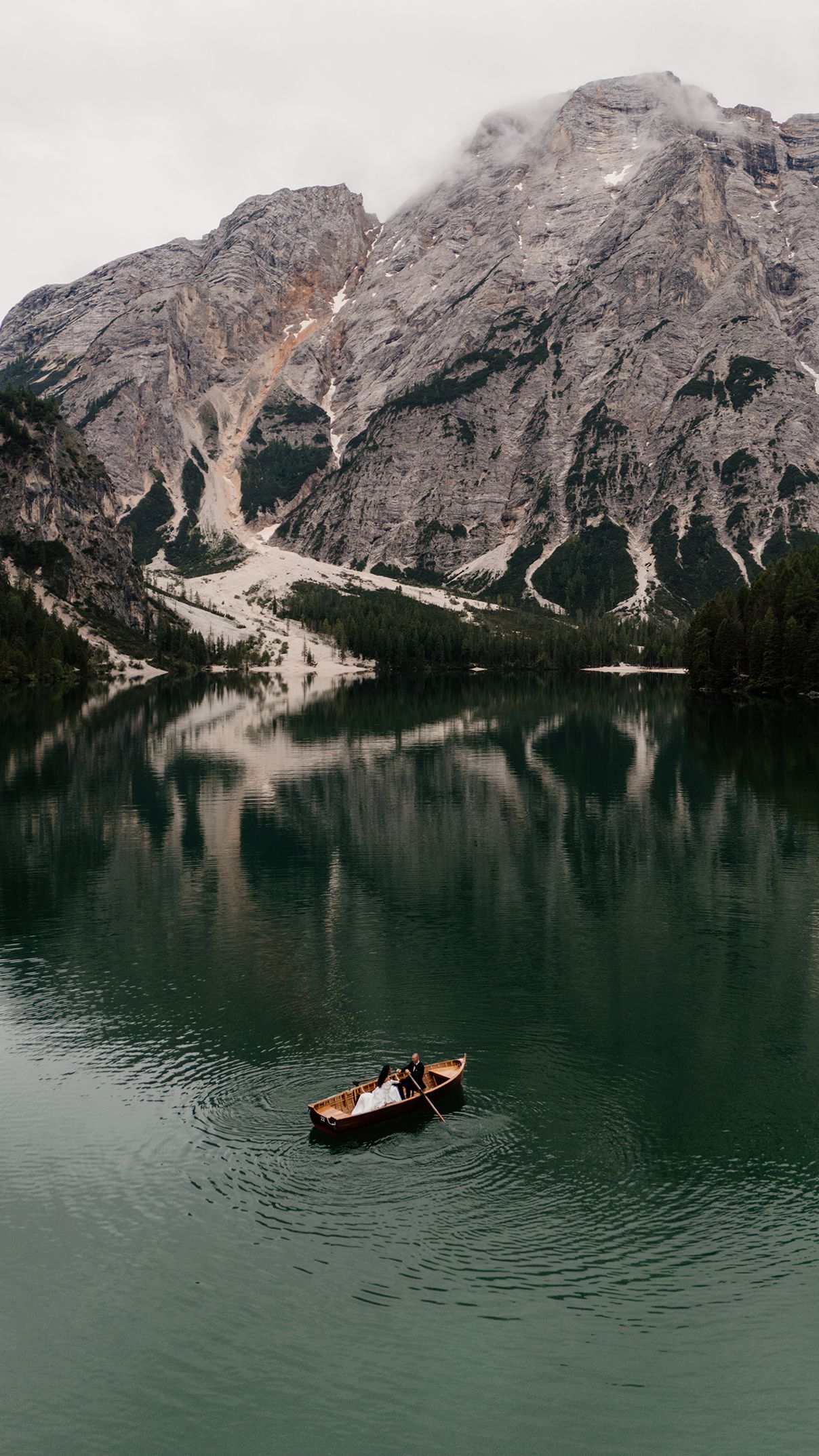 Couple in rowboat on serene alpine lake with dramatic mountain reflection in Dolomites Italy.
