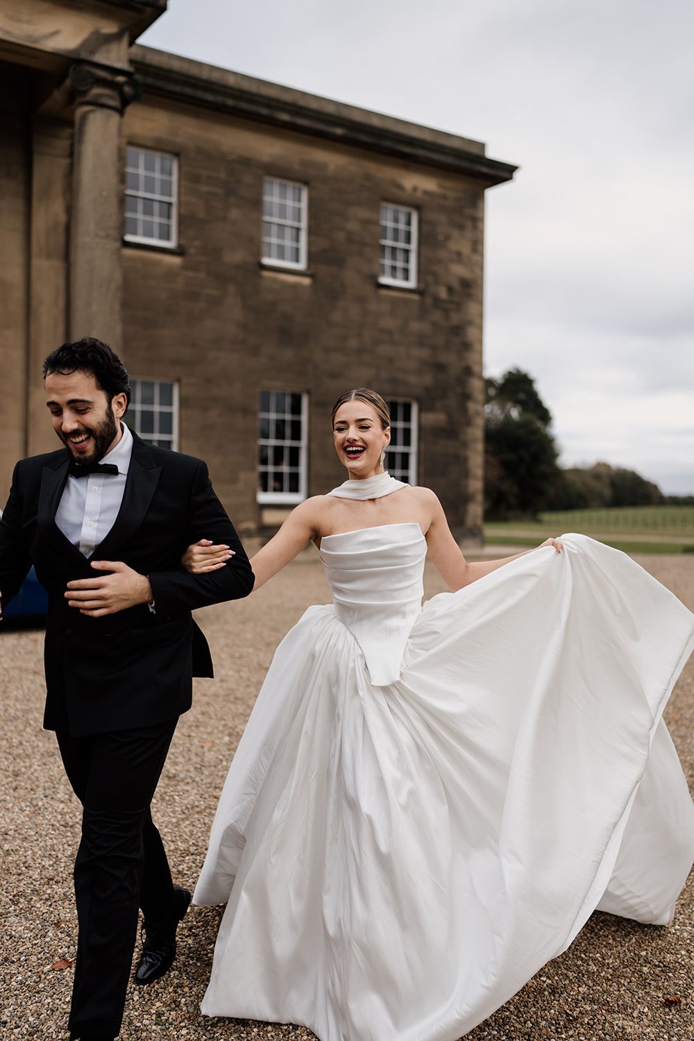 Bride and groom running in the grounds of Rise Hall, holding autumnal flowers while laughing and smiling.