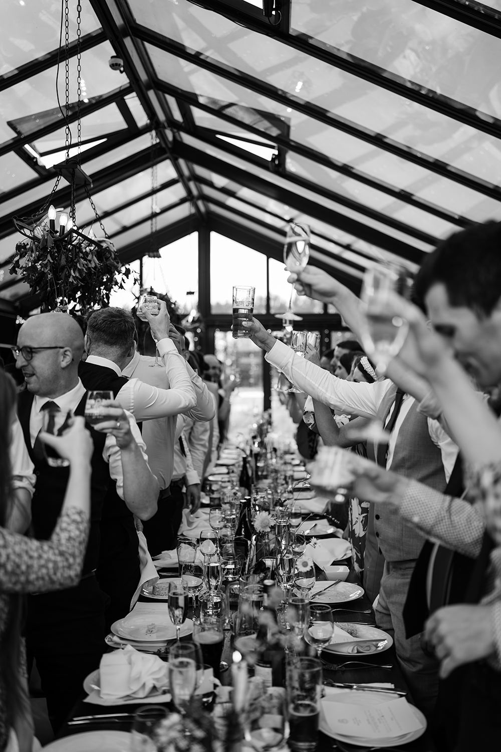 Wedding guests stood cheering with wine glasses and beer glasses celebrating after wedding speeches.