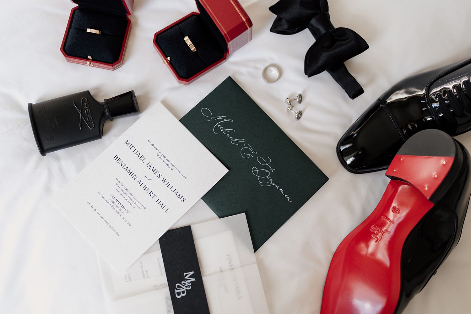 Grooms wedding rings, stationery, shoes, aftershave and wedding rings on a white background.