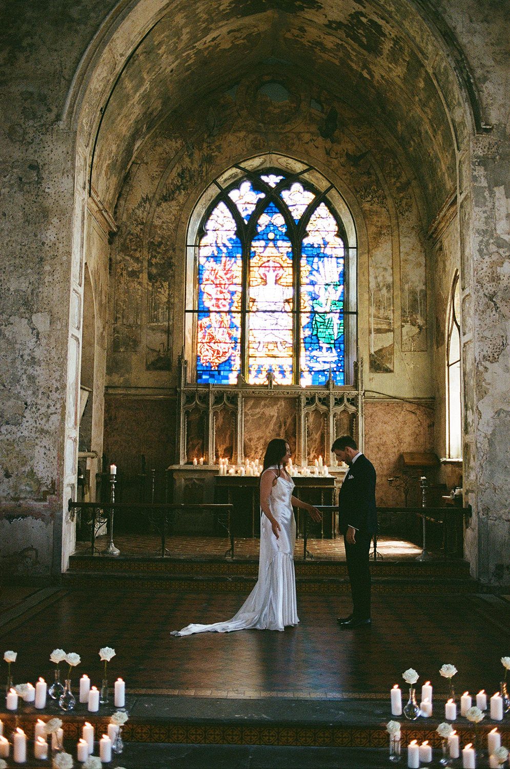 A panoramic view of a historic church interior with stained glass windows and candles lining the aisle during a ceremony.