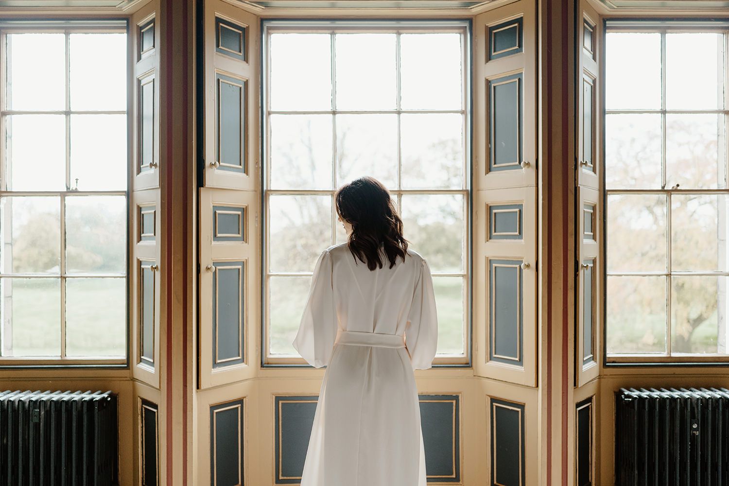 Bride looking out of window in her wedding morning gown at Rise Hall.