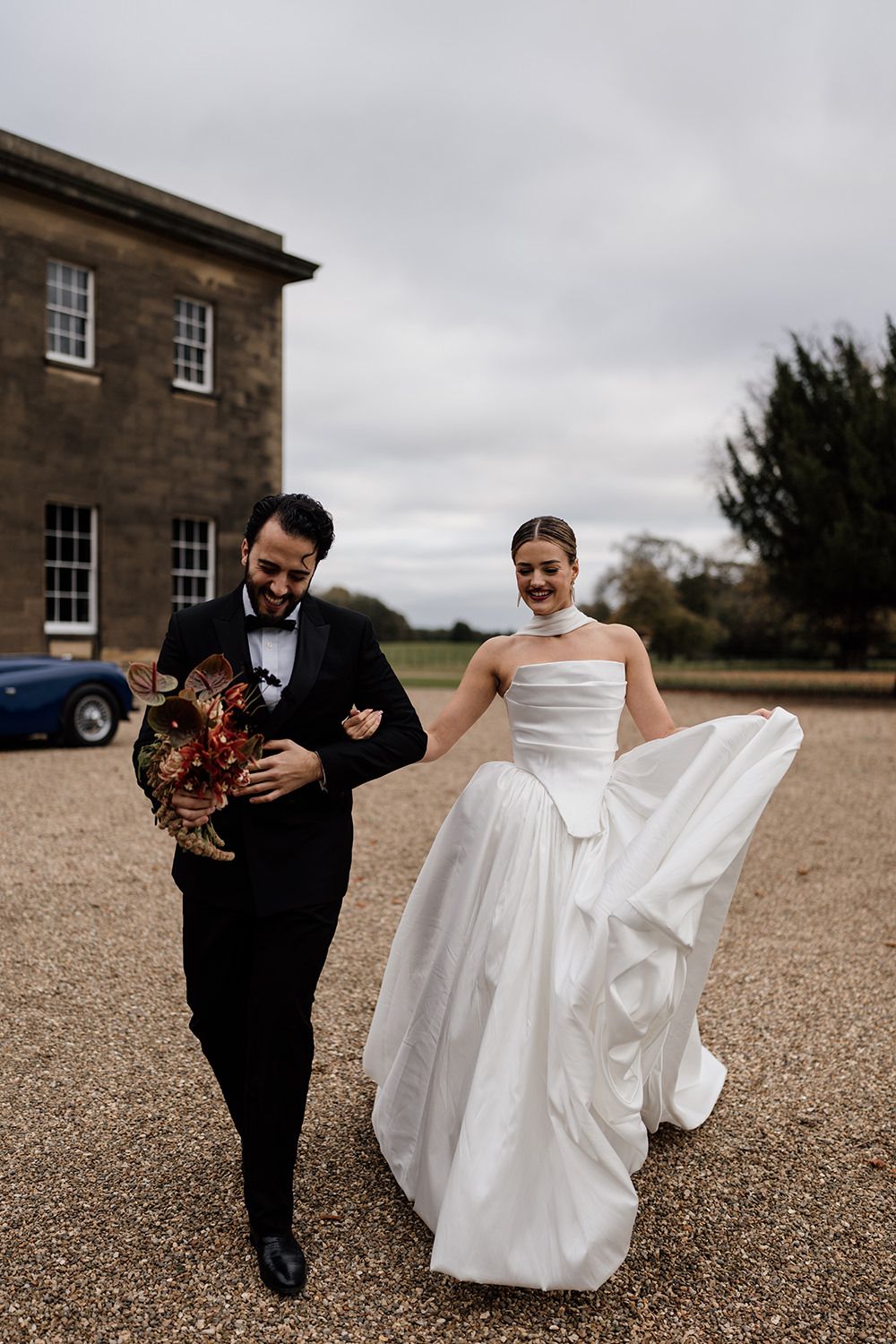 Bride and groom running in the grounds of Rise Hall, holding autumnal flowers while laughing and smiling.