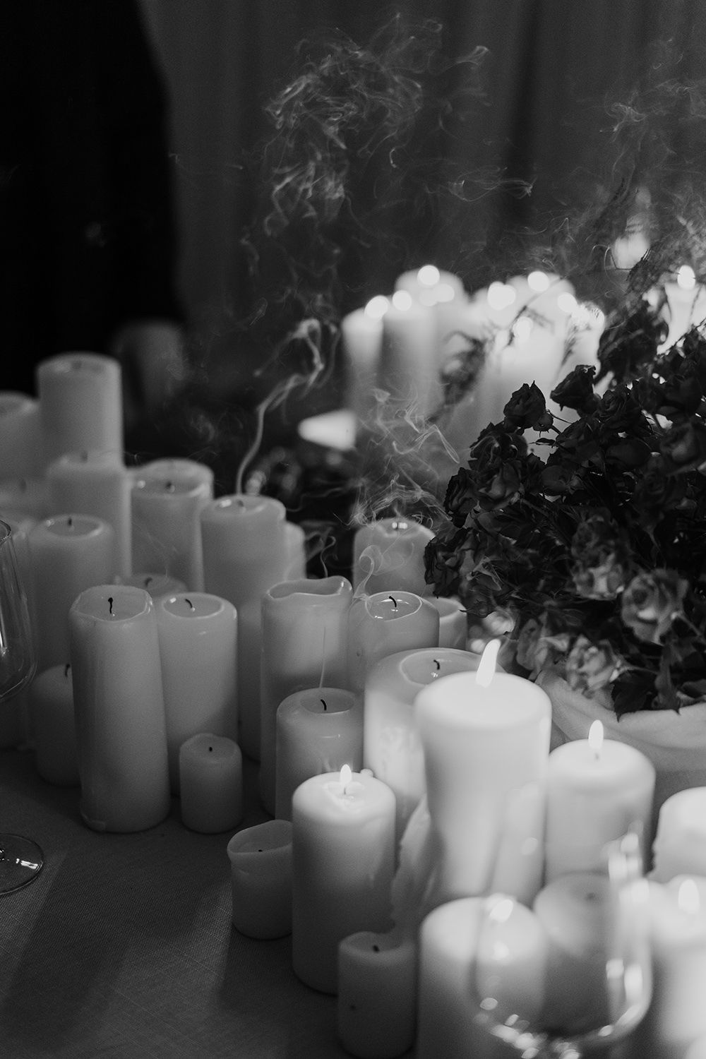 Multiple extinguished white candles in a row emit wisps of smoke in a dramatic black and white composition.