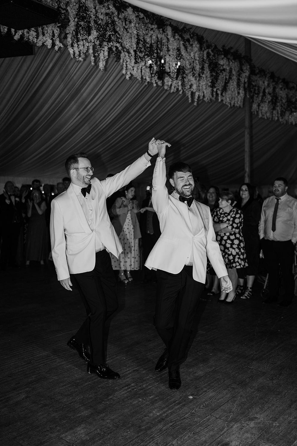 Grooms first dance together while guests watch in black and white.