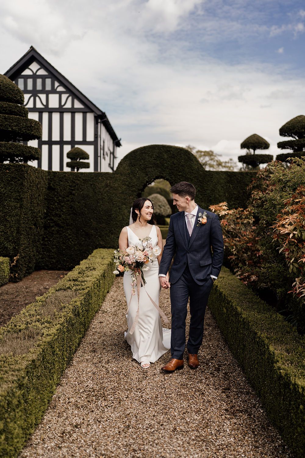 Bride and Groom walking and smiling through the gardens at The Holford Estate surrounding them.