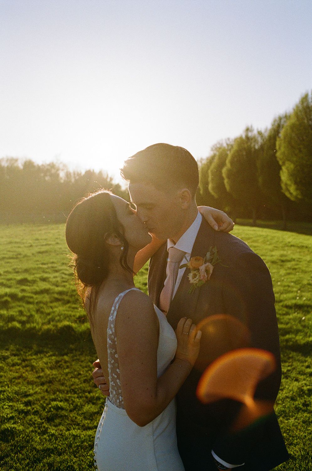 Bride and groom kissing with sun setting behind them on 35mm film.
