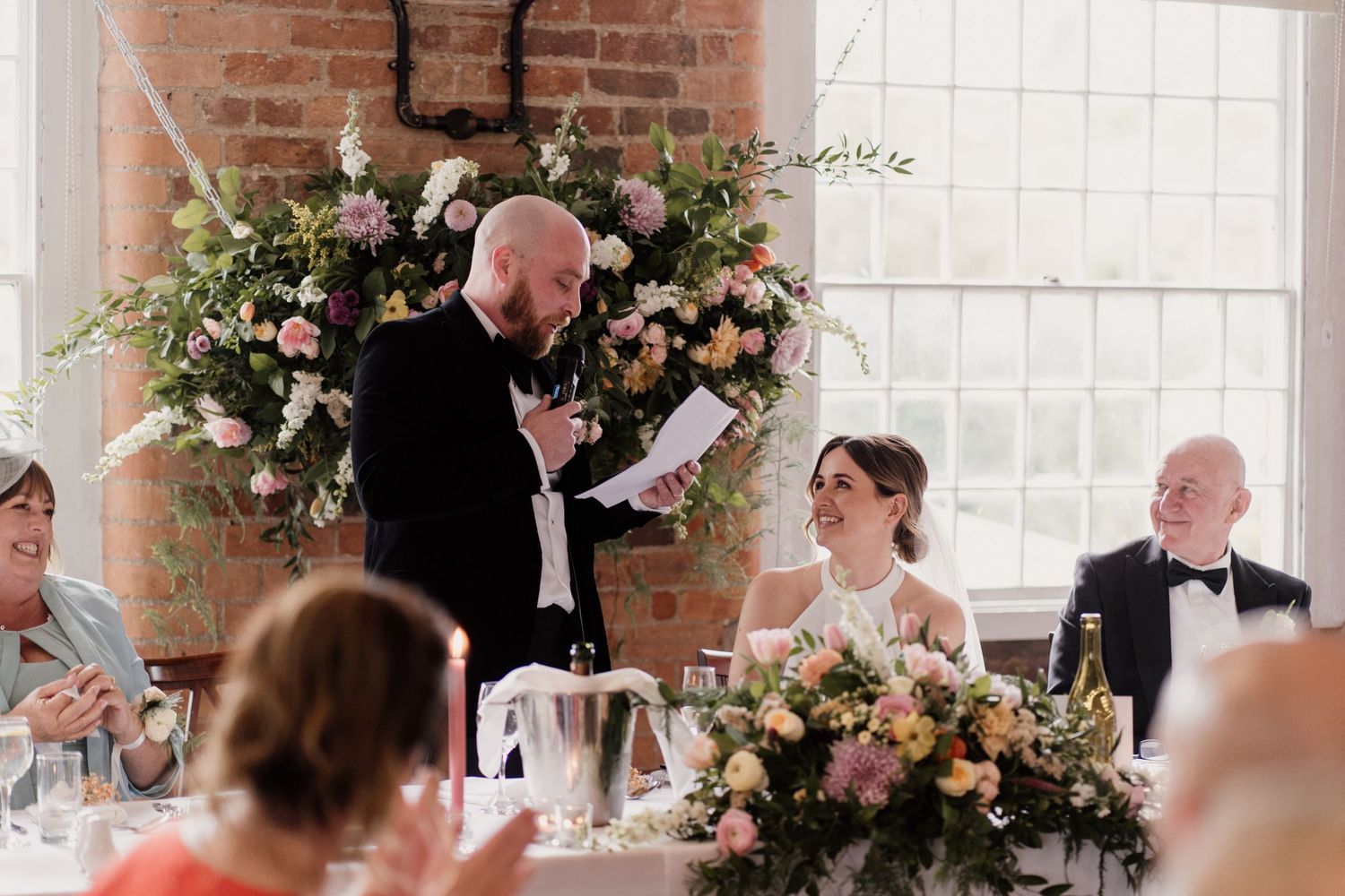 Wedding reception toast being delivered with beautiful pink and white floral arrangements.