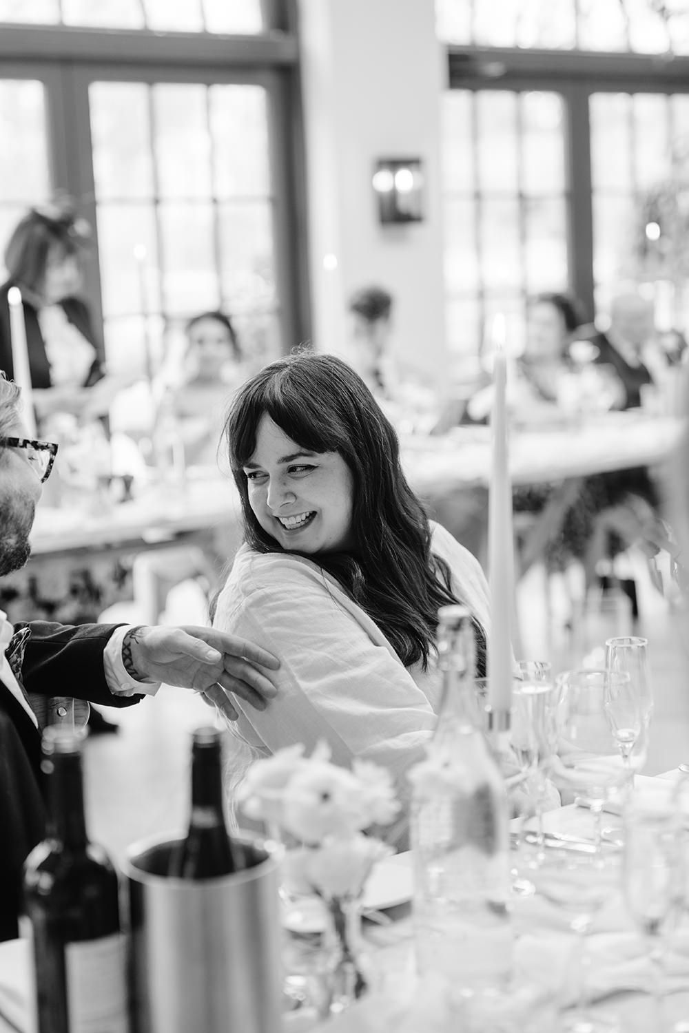 Black and white photo of a celebration around a formal dining table with wine bottles and glassware.
