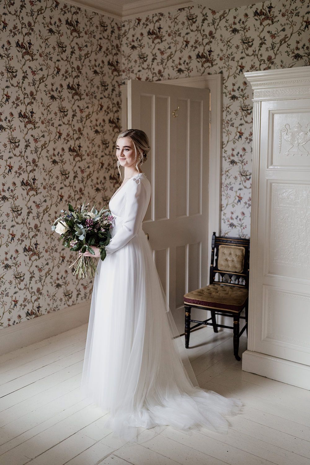 Bride in wedding dress looking out of the window while she holds her bouquet.