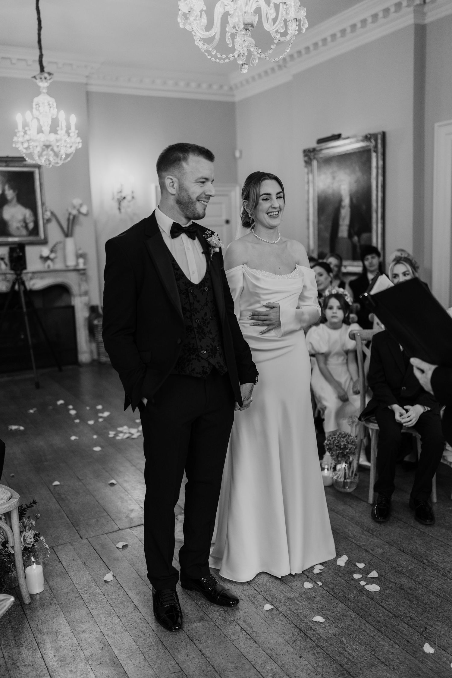 A couple shares a joyful moment during their wedding ceremony in an elegant room with crystal chandeliers.