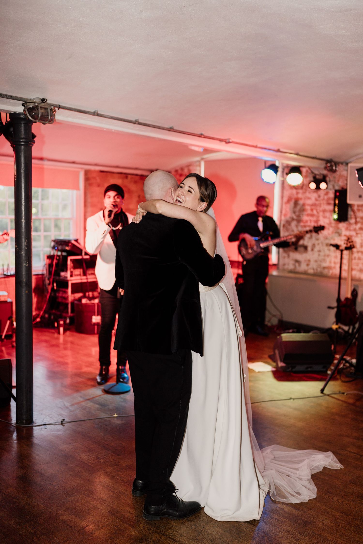 Newlyweds dancing in reception venue with pink lighting and live band performing.