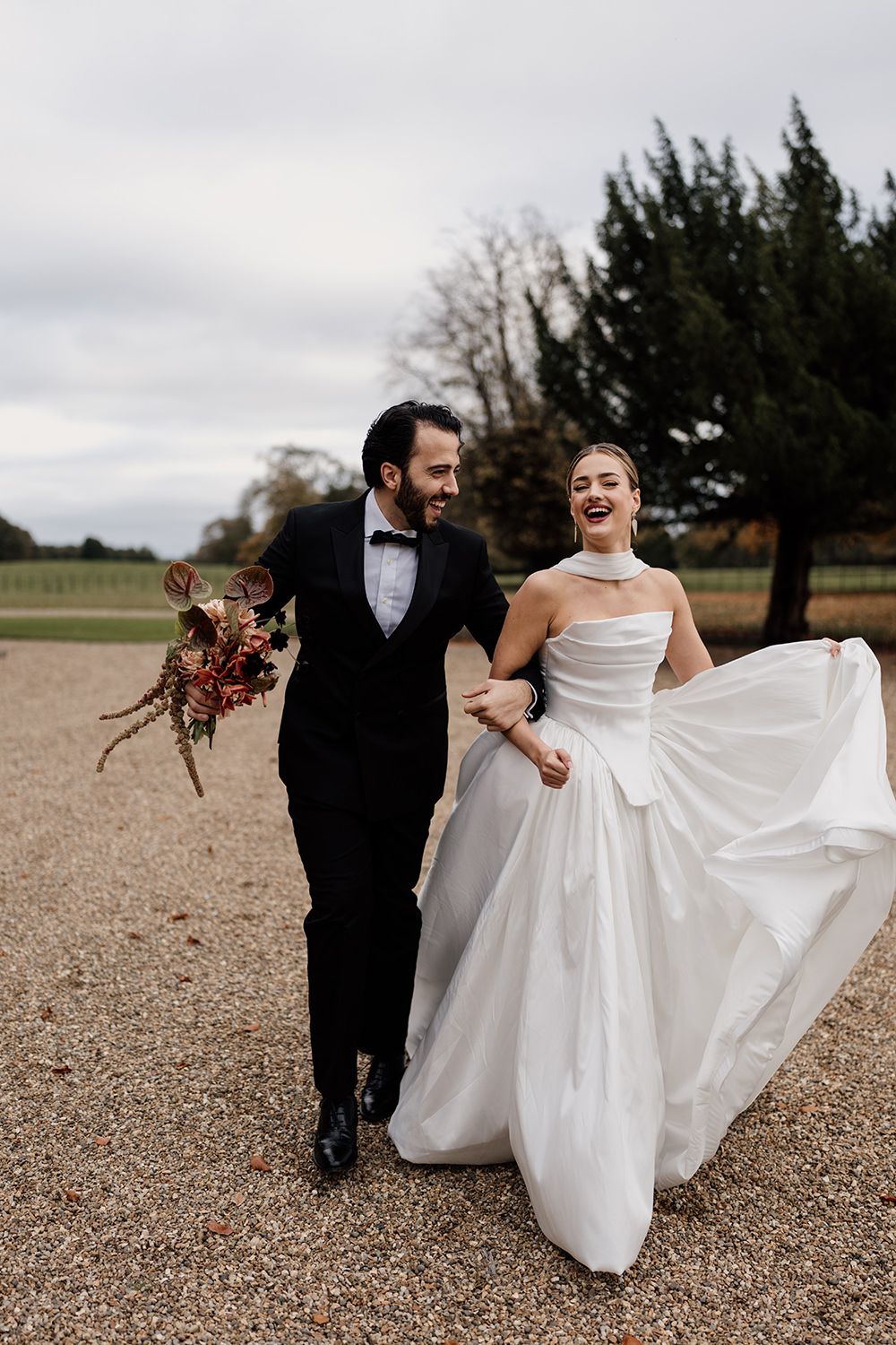 Bride and groom running in the grounds of Rise Hall, holding autumnal flowers while laughing and smiling.