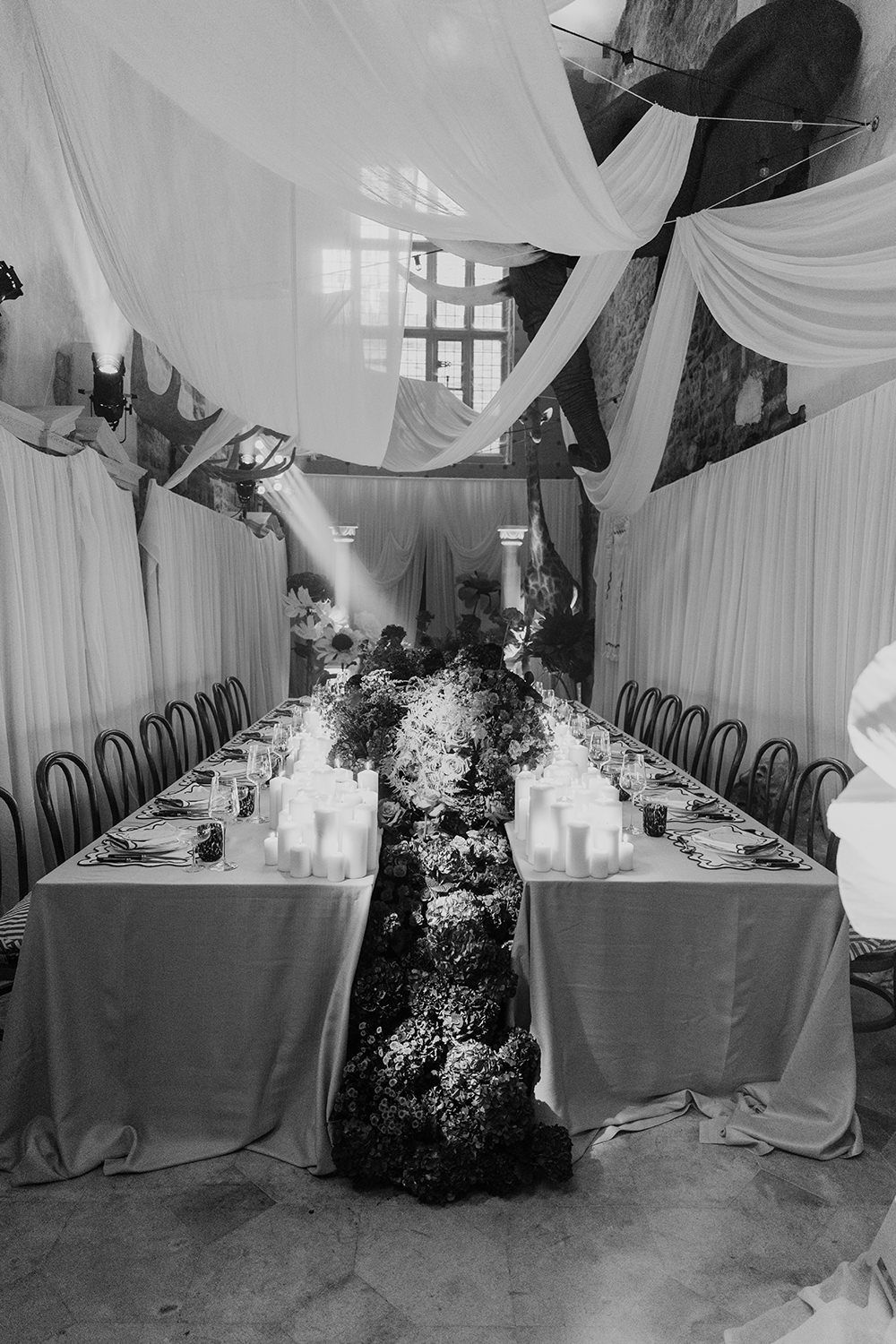 Black and white wedding reception table setup with draped white fabric ceiling and two long tables adorned with florals and candles.