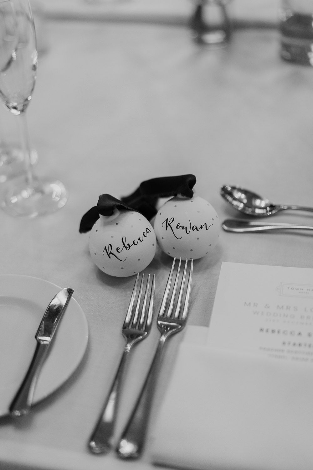 Black and white photo of wedding place settings with name cards written on ornate baubles with matching cutlery and menu card.