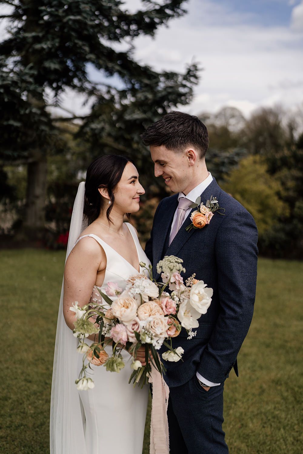 Bride and groom stood looking at each other smiling, the bride is holding her wedding bouquet.