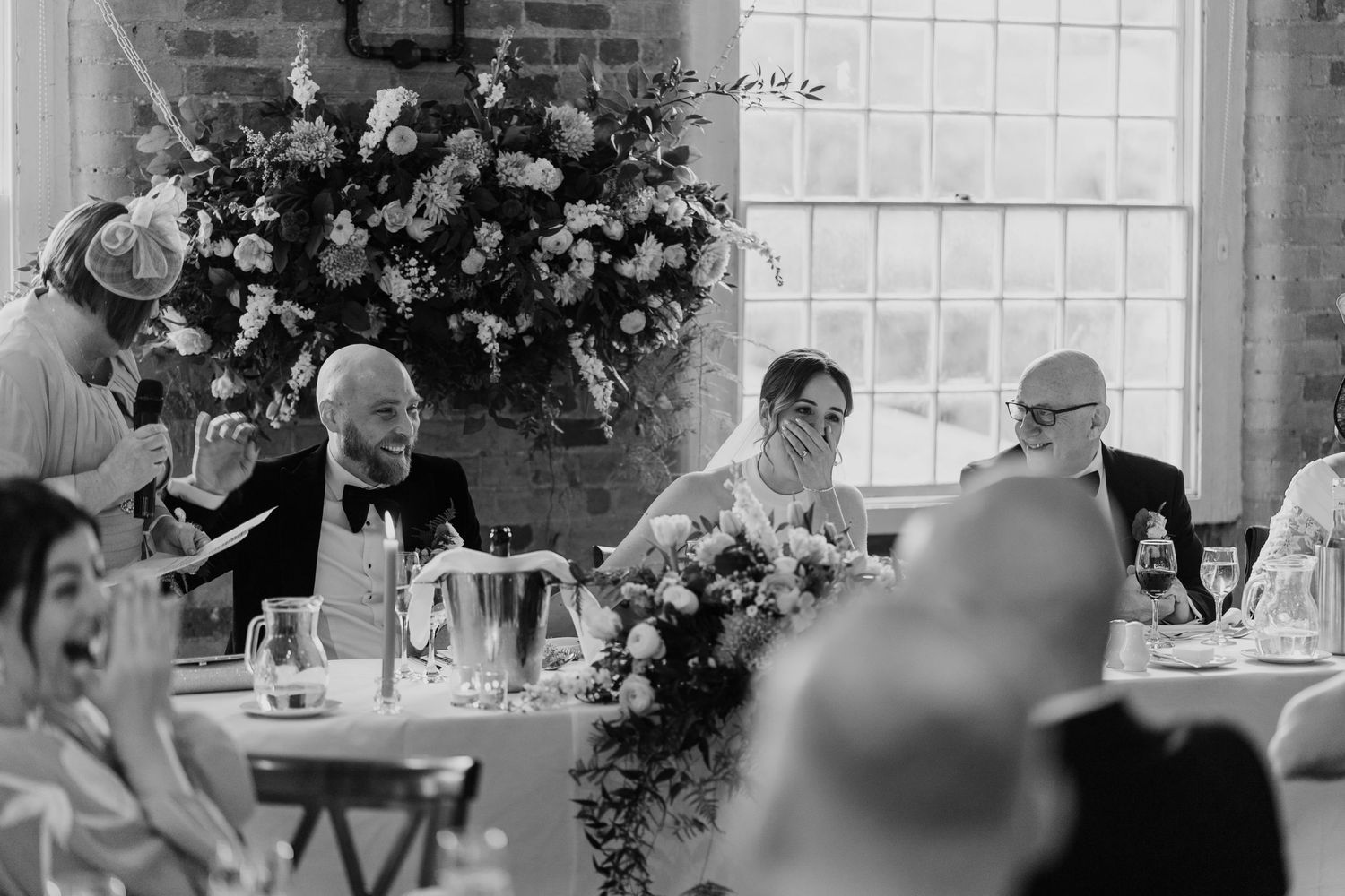 Black and white photo of reception dinner with elegant floral arrangements and formal table settings.