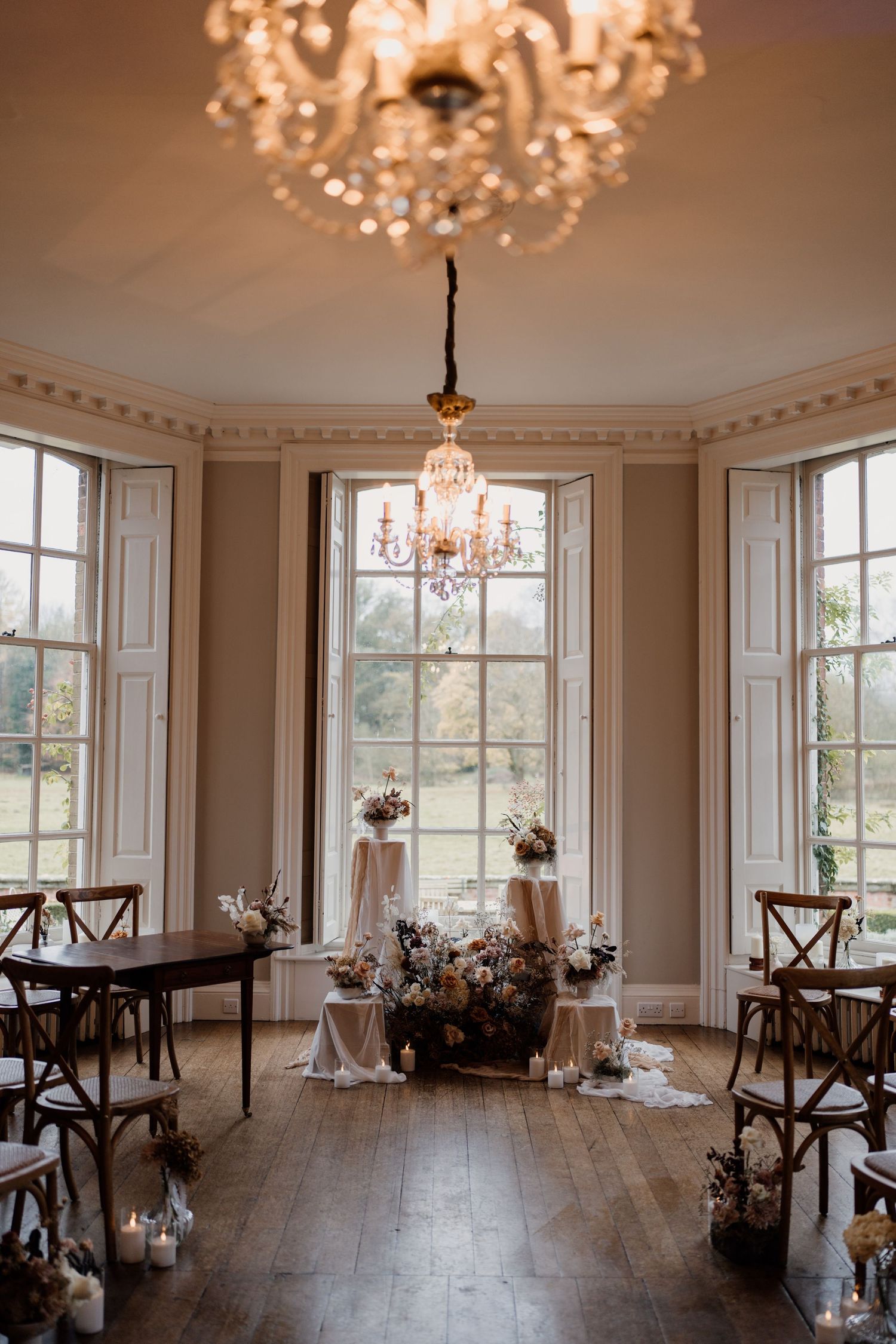 Elegant wedding ceremony setup in a bright room with chandelier, hardwood floors and tall windows.