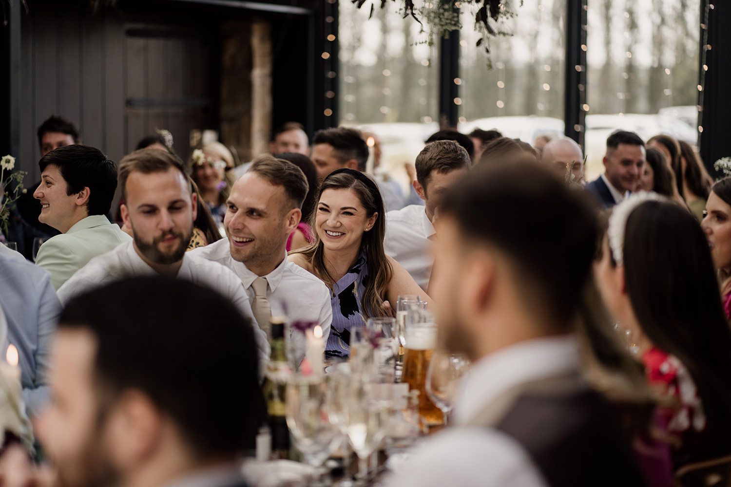 Wedding guest smiling sitting amongst other guests during speeches at the Hovels Harewood.