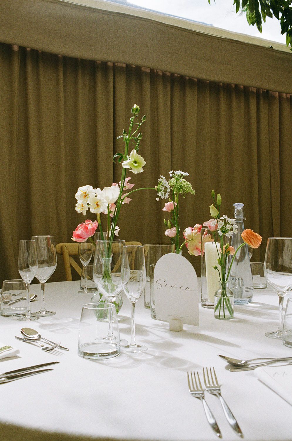 35mm film image of wedding reception table, there are flowers in glass vases and crockery.