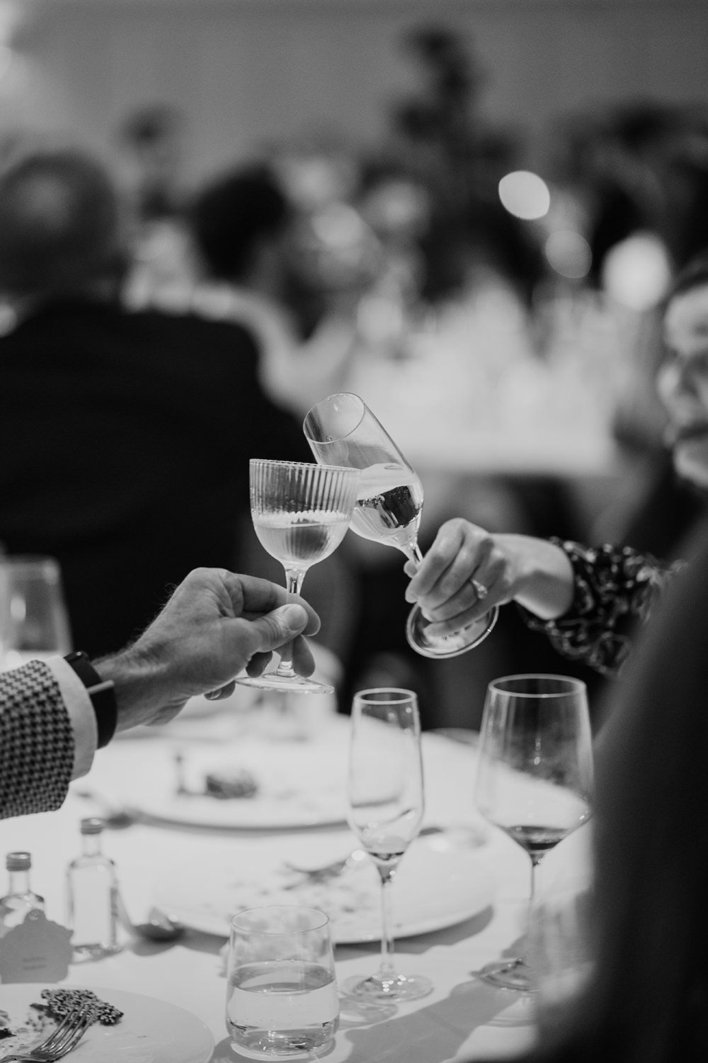Black and white photo of hands toasting with wine glasses at elegant dinner table during celebratory gathering.