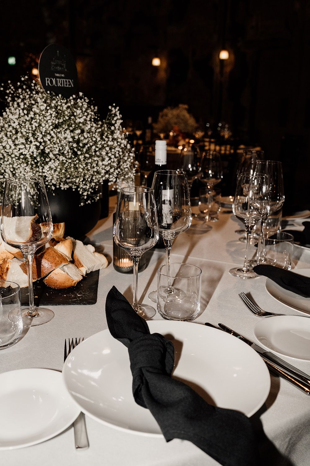 Elegant wedding reception table setting with white plates, black napkins and baby's breath floral arrangements.