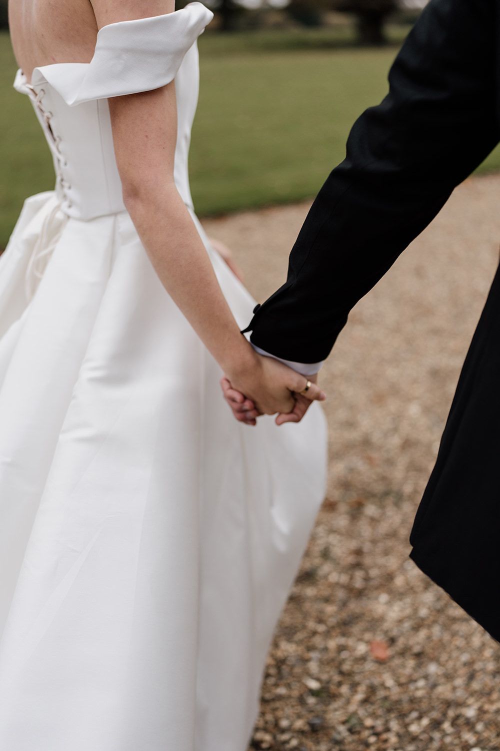 A detail photograph of a bride and groom holding hands, smiling, laughing while working through the grounds of Rise Hall.