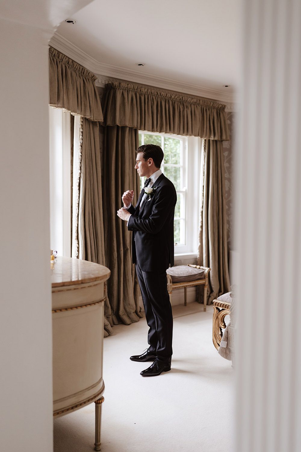 A series of photos showing a person in a black suit standing by a window in a bright white room with beige curtains.